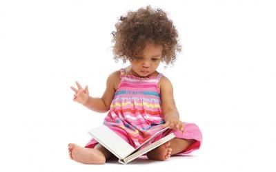 Peuter met krullen leest een kleurrijk prentenboek op de grond